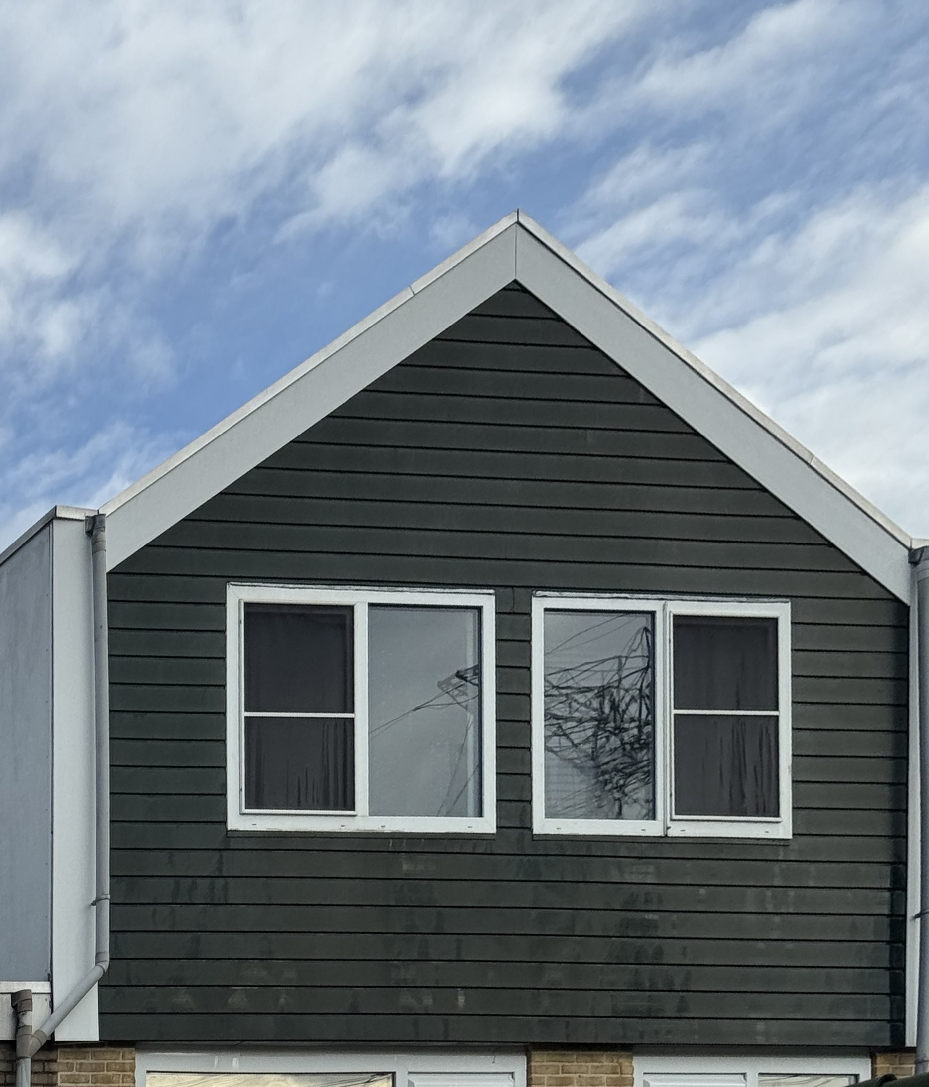 Woninggevel met donkergroene bekleding en witte kozijnen onder een blauwe lucht